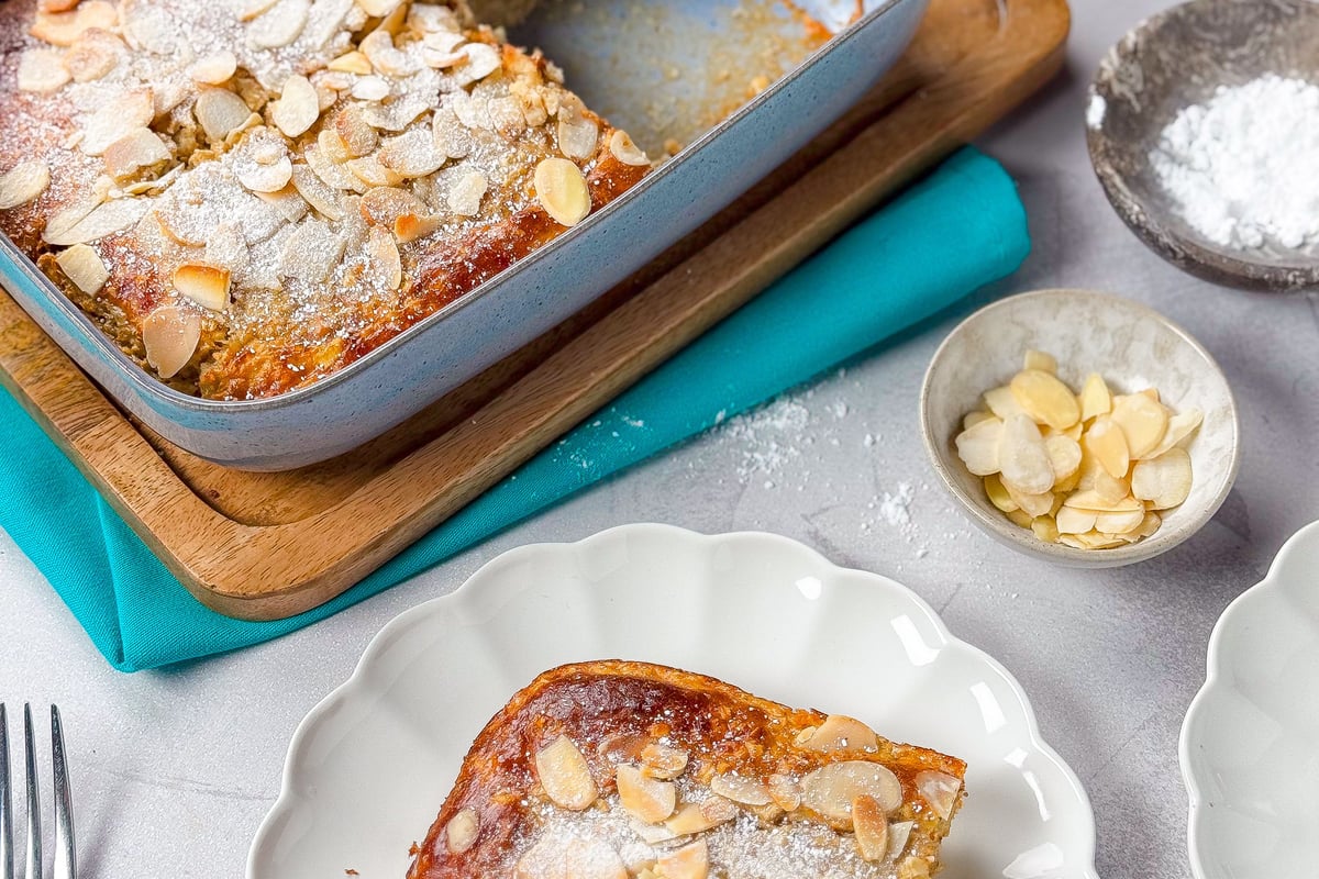 Baked almond cake with powdered sugar in a blue baking dish and a slice on a white plate