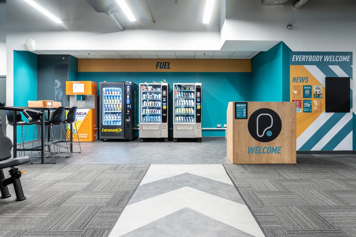 PureGym Ipswich Buttermarket: Seating area with high tables and stools, a welcome podium, and food and beverage vending.