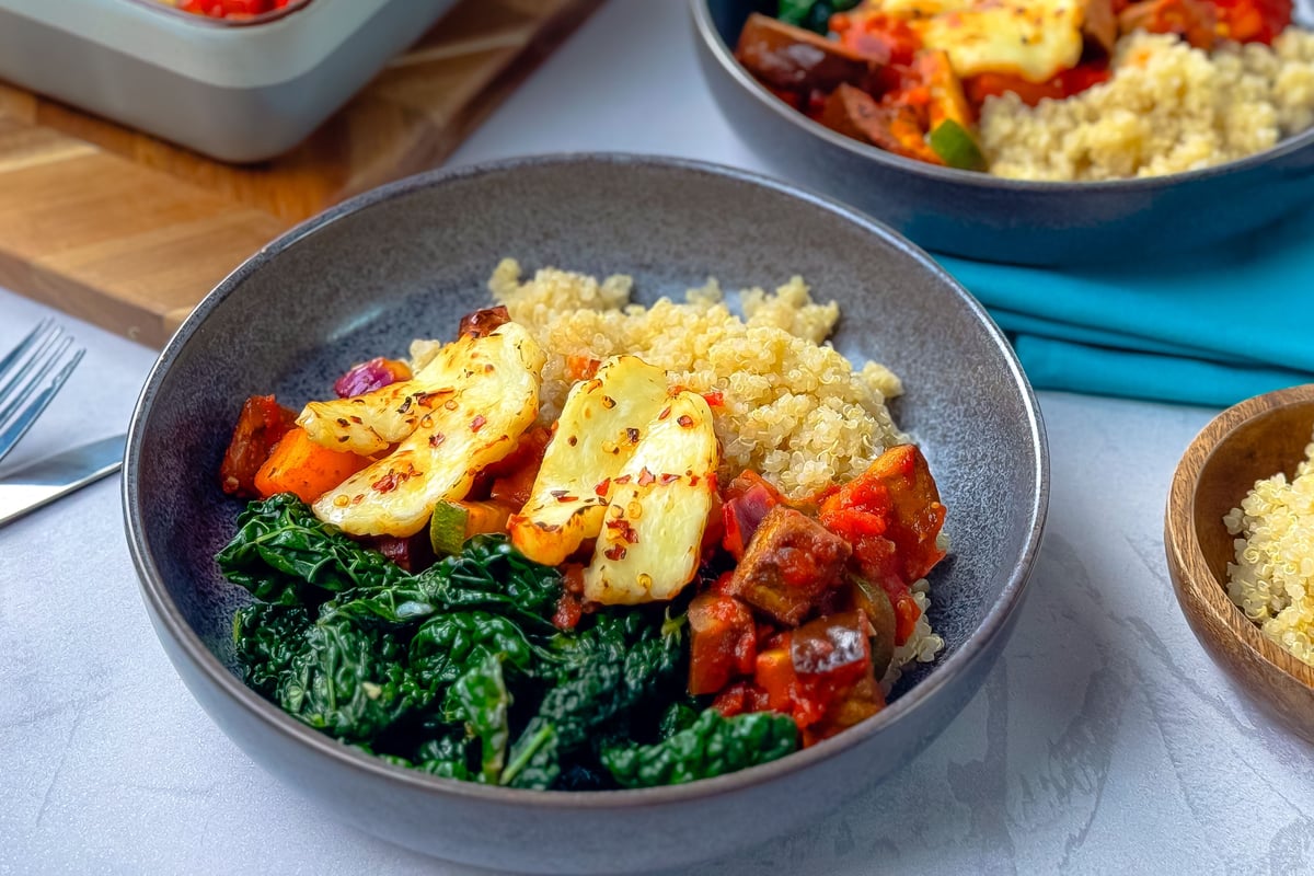 Grey bowl containing quinoa, roasted vegetables, greens and halloumi cheese
