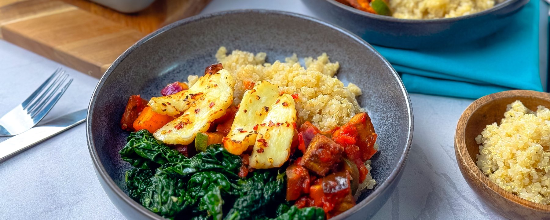 Grey bowl containing quinoa, roasted vegetables, greens and halloumi cheese