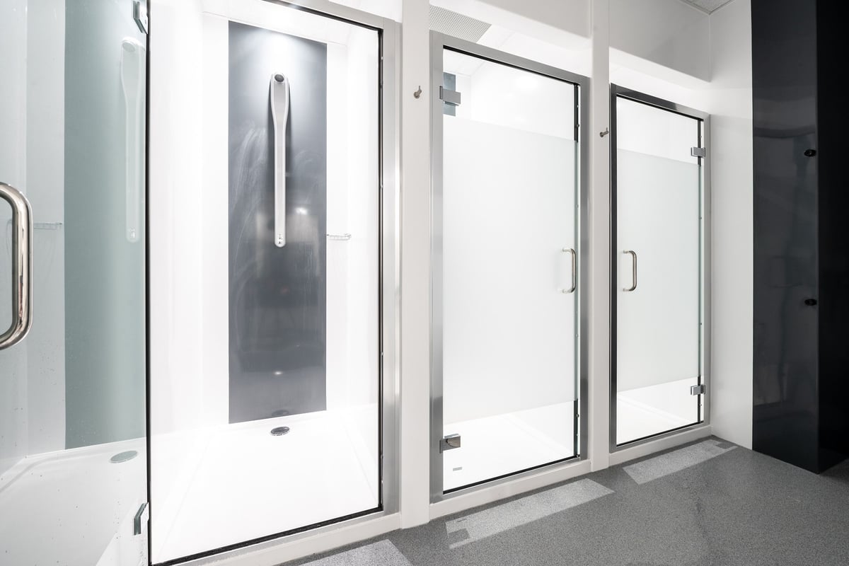 PureGym Aldershot Westgate Retail Park: Rows of glass-enclosed shower stalls or changing rooms with benches.