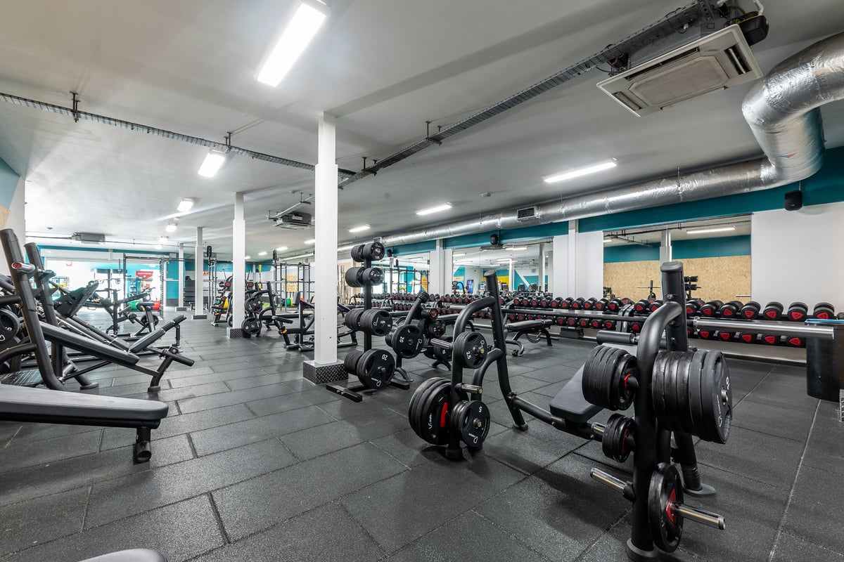 PureGym Ashton Under Lyne: Strength training area with weight machines, benches, dumbbells, and weight plates.