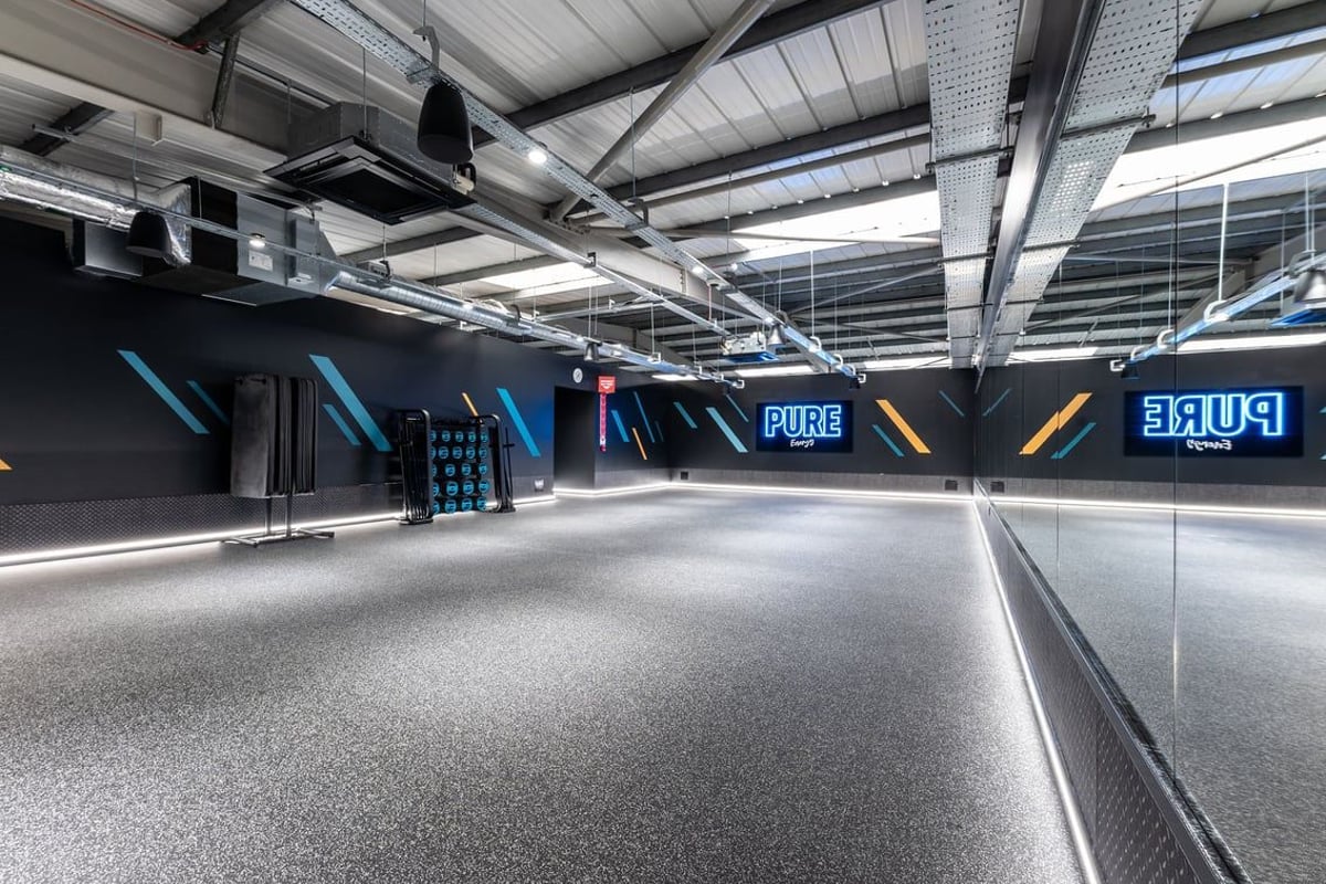 PureGym Dagenham: Bright studio space with rubberized flooring, mirrors, weight racks, and neon signage.