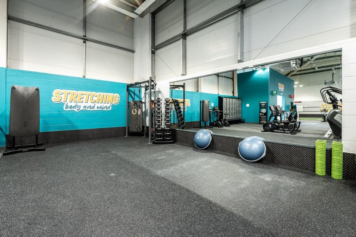 PureGym Newbury: Stretching area with medicine balls, foam rollers, kettlebells, wall graphics, and rubberized flooring.