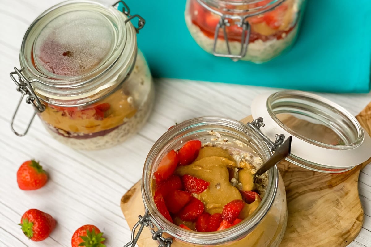 Three jars with overnight oats topped with peanut butter and strawberries on a white table