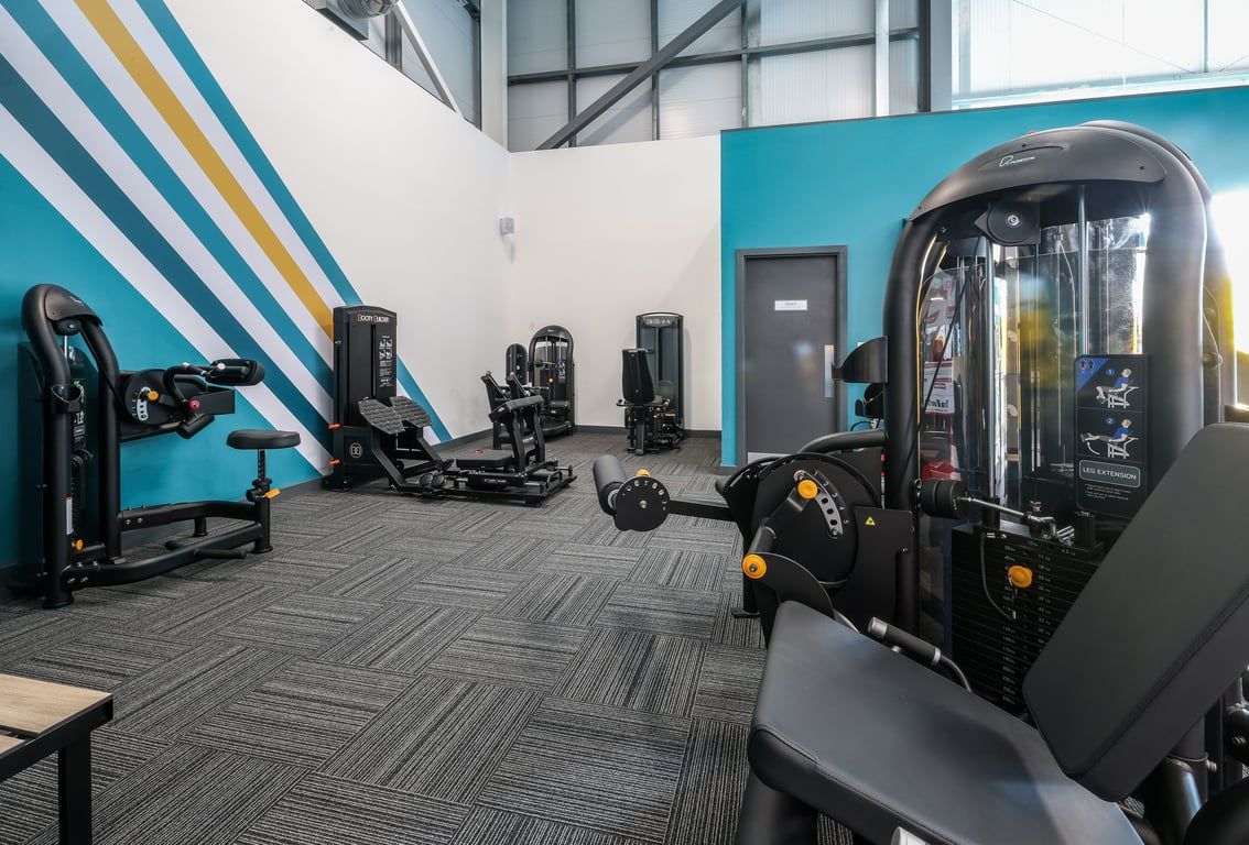 PureGym Bishop Auckland: Resistance machines, a VR rig, rubberized flooring, and striped accent wall inside a gym studio.