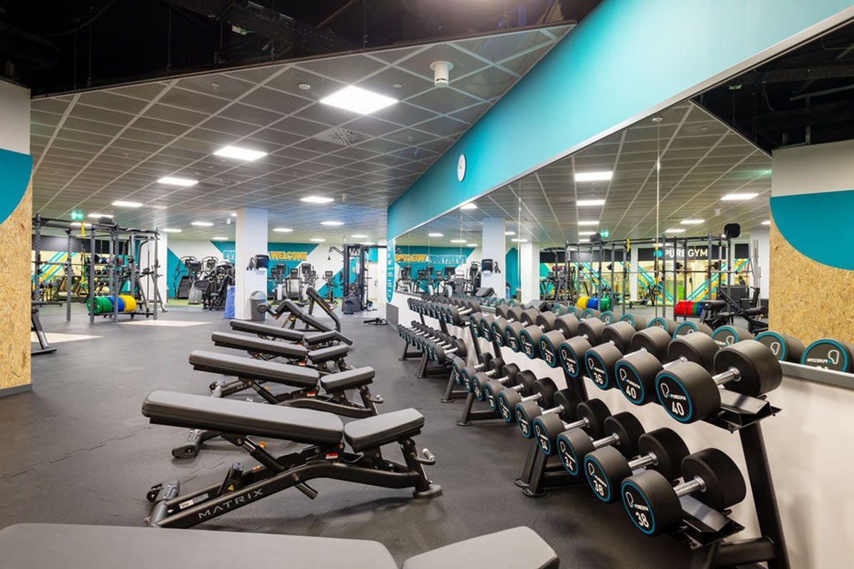 PureGym Lausanne Prilly: Gym with weight benches, dumbbells, treadmills and resistance machines in teal and white interior.