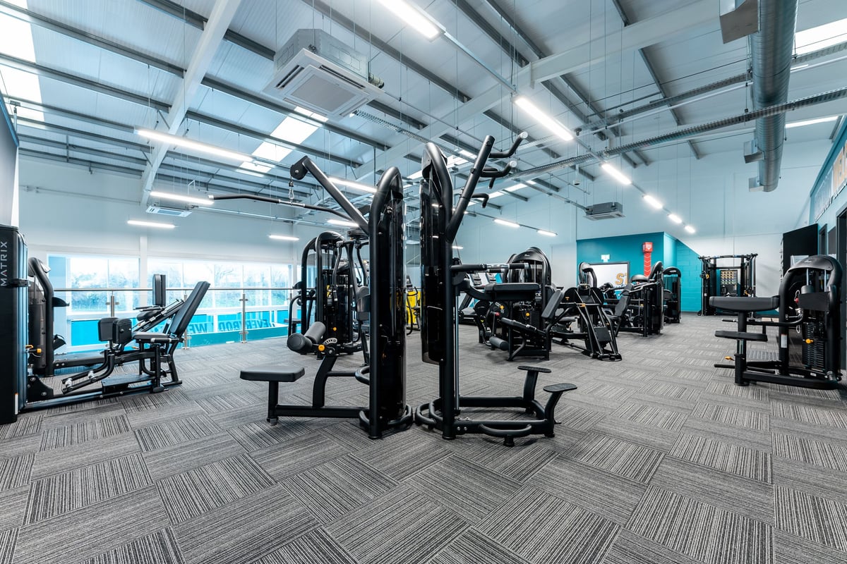 PureGym Caerphilly: Weight machines, benches, weights, mirrored walls, and rubberised flooring inside a gym studio.