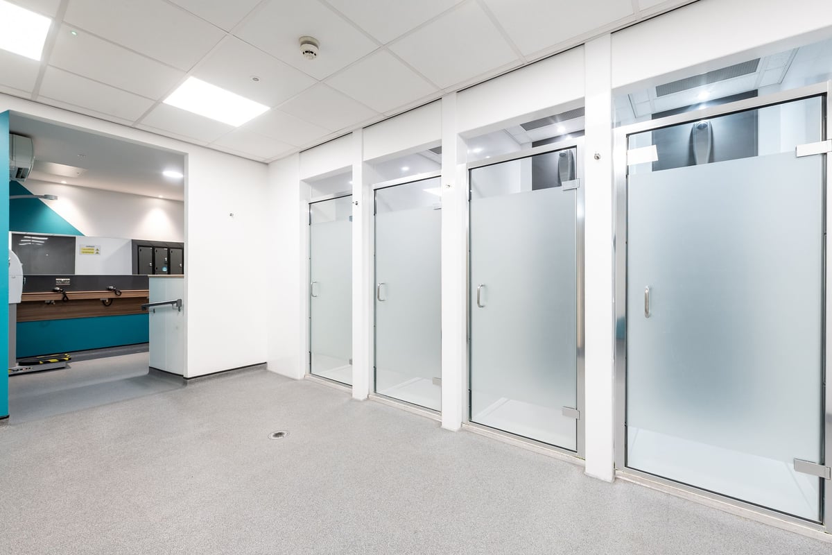 PureGym London Limehouse: Changing rooms with frosted glass cubicles, tiled flooring.