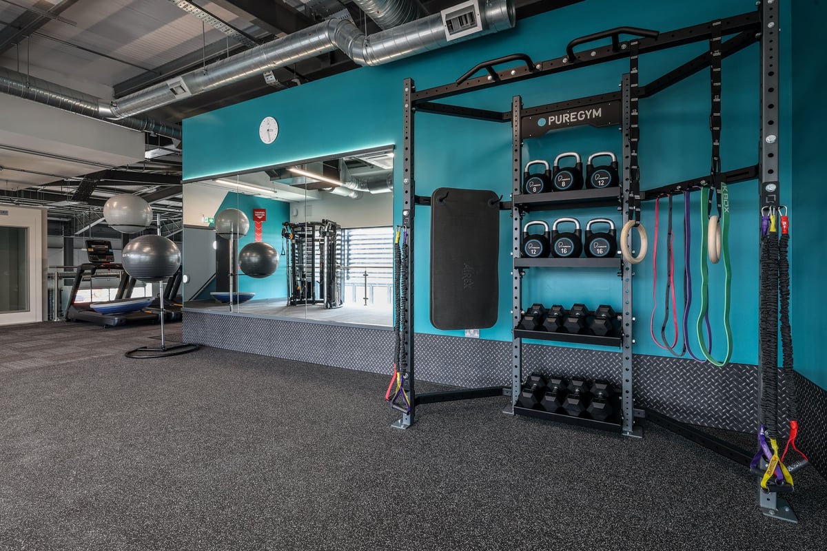 PureGym Bishop Auckland: Gym with weight racks, medicine balls, battle ropes, rubberized flooring, and teal accent walls.