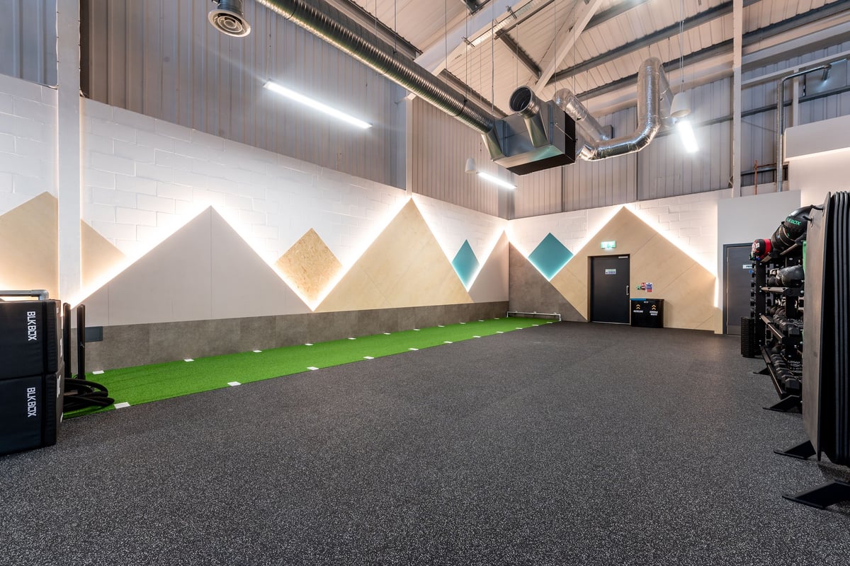 PureGym Spalding: Pyramid-shaped padded structures, green turf, weight racks, rubberized flooring in a gym studio.
