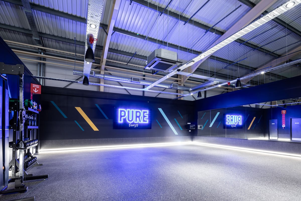 PureGym Neath: Neon-lit studio space with pure branding and rubberized flooring.