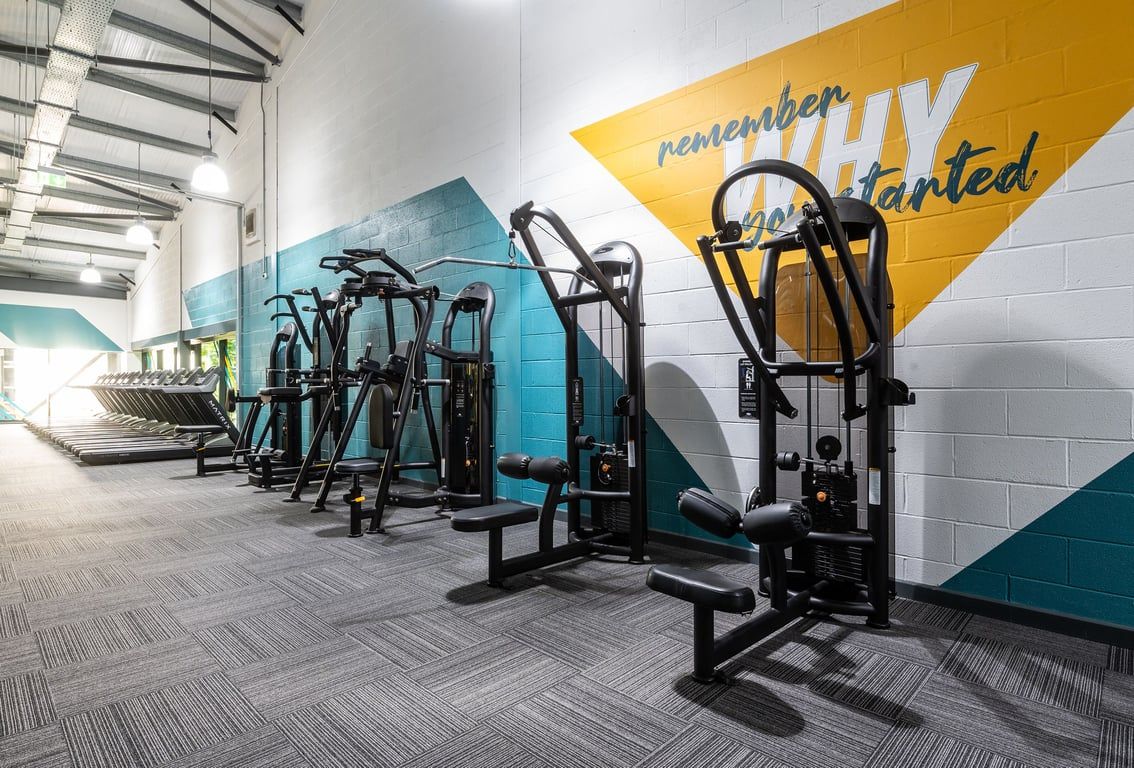 PureGym Banbury Cross Retail Park: Rows of modern resistance training machines with cable pulleys, on rubberized flooring.