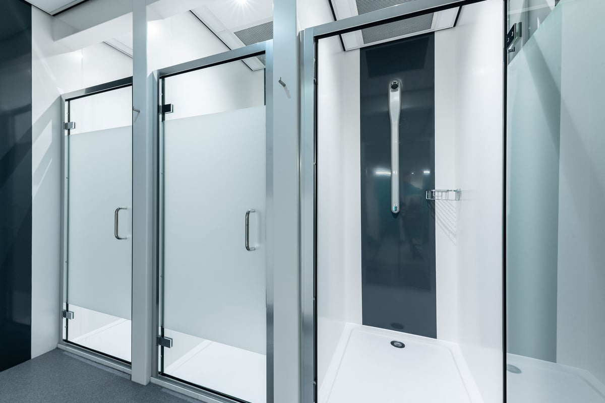 PureGym Byfleet: Glass shower stalls, chrome handles, tiled floor - appears to be a changing room or shower facility.