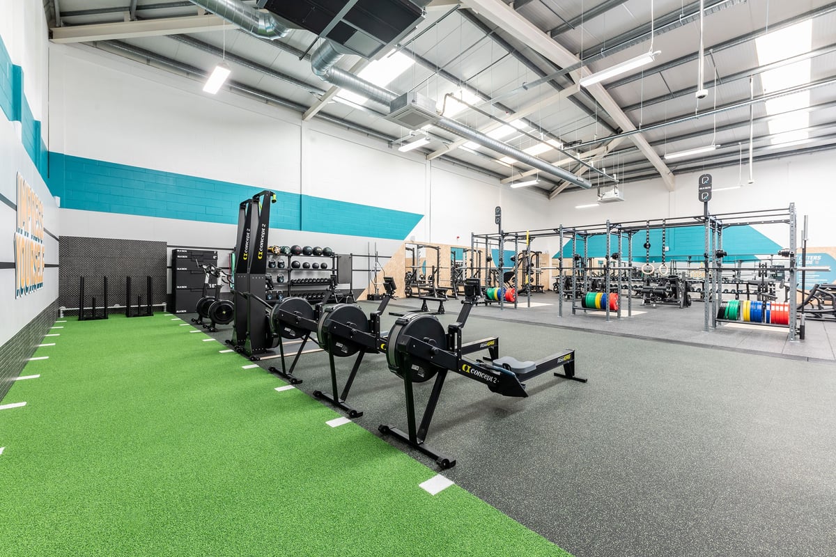 PureGym Dumfries: Squat racks, prowlers, weightlifting platforms on rubberized green and grey flooring.