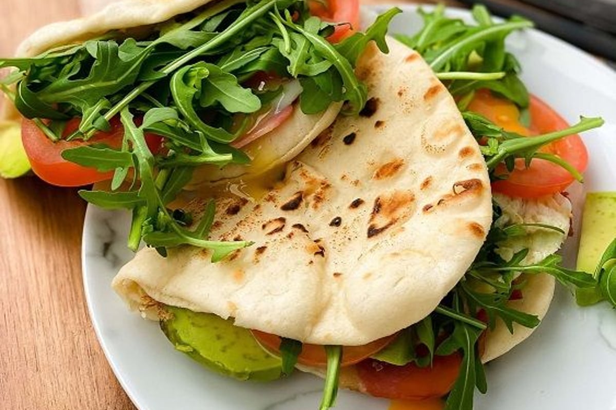 Flatbread sandwiches filled with arugula, tomato slices, and avocado on a white plate.