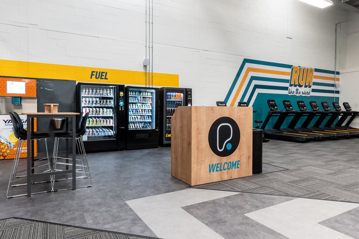 PureGym Dagenham: Rows of drink fridges, snack vending machines, a welcome desk and geometric seating area.