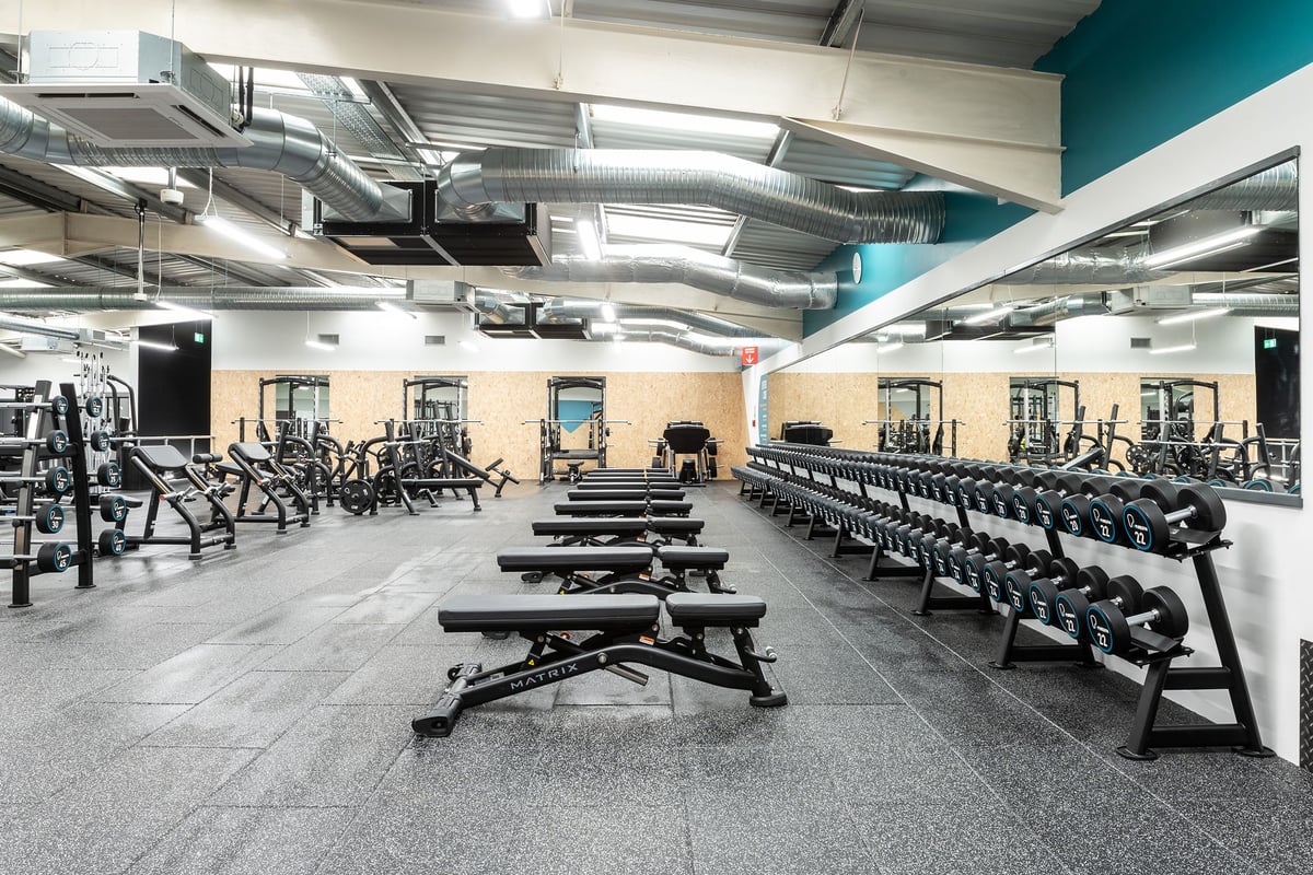 PureGym Cardiff Western Avenue: Rows of weight benches, squat racks, dumbbells, and exercise machines with mirrored walls.