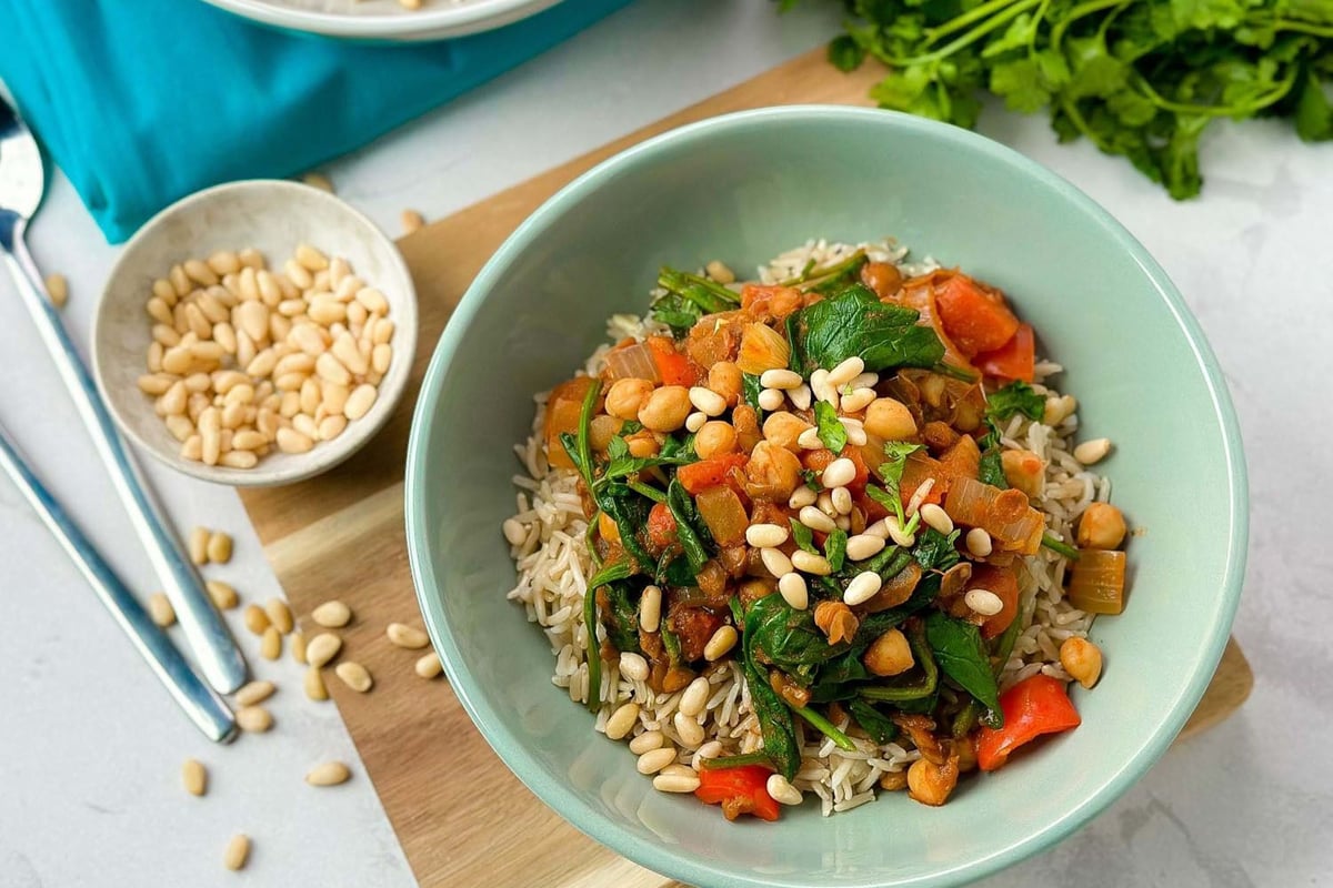 Bowl of rice topped with chickpeas, spinach, red peppers, and pine nuts on a wooden board