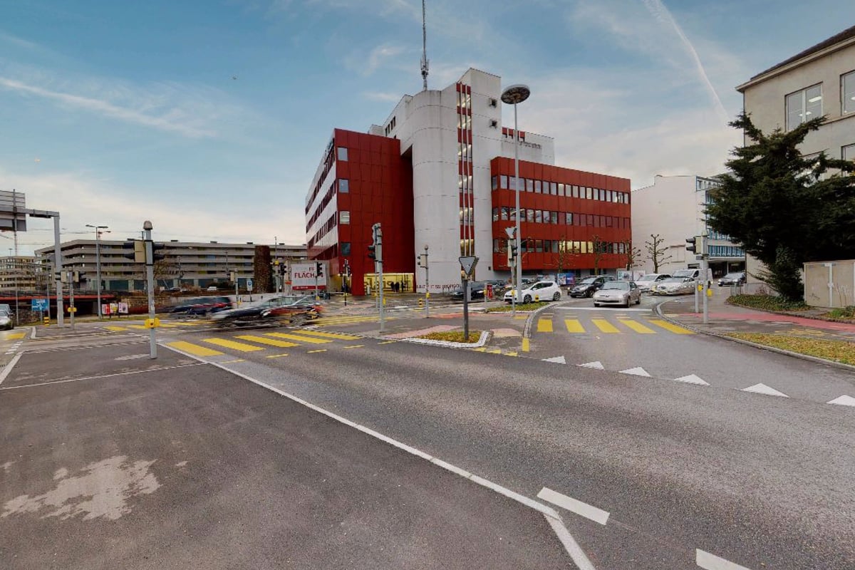 PureGym Aarau: Bâtiment extérieur avec parking, marquage routier et immeuble de bureaux en briques rouges en arrière-plan.