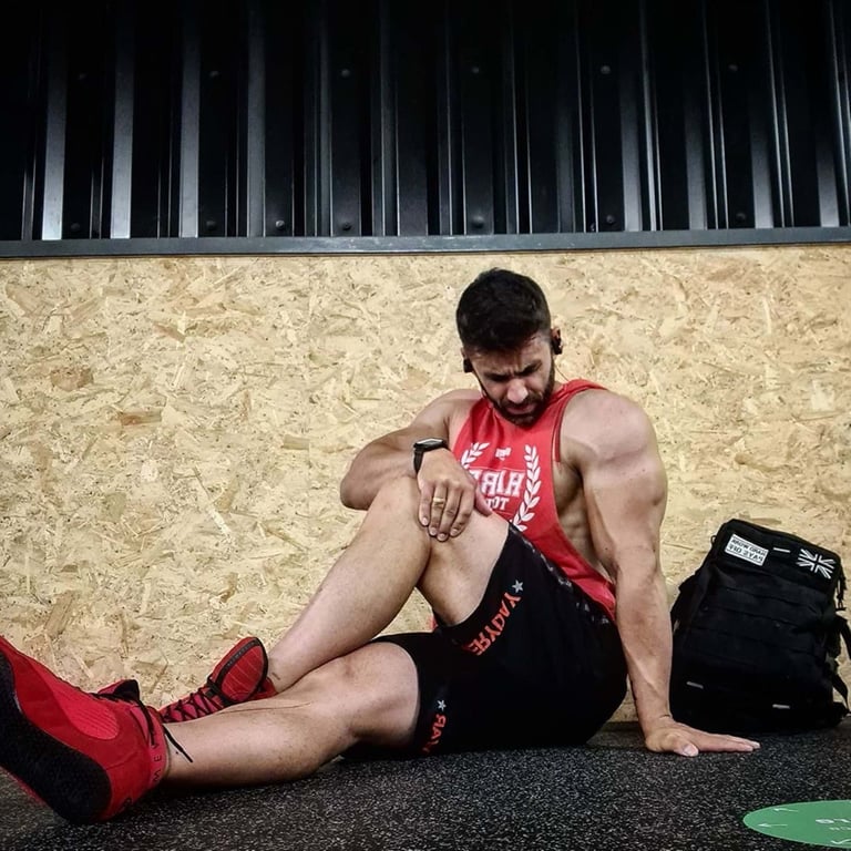 Man in red vest and black shorts sitting on gym floor stretching leg muscles