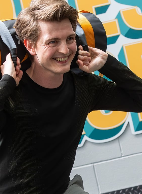 Lächelnder Mann trägt einen Sandsack auf den Schultern vor einer bunten PureGym-Wand