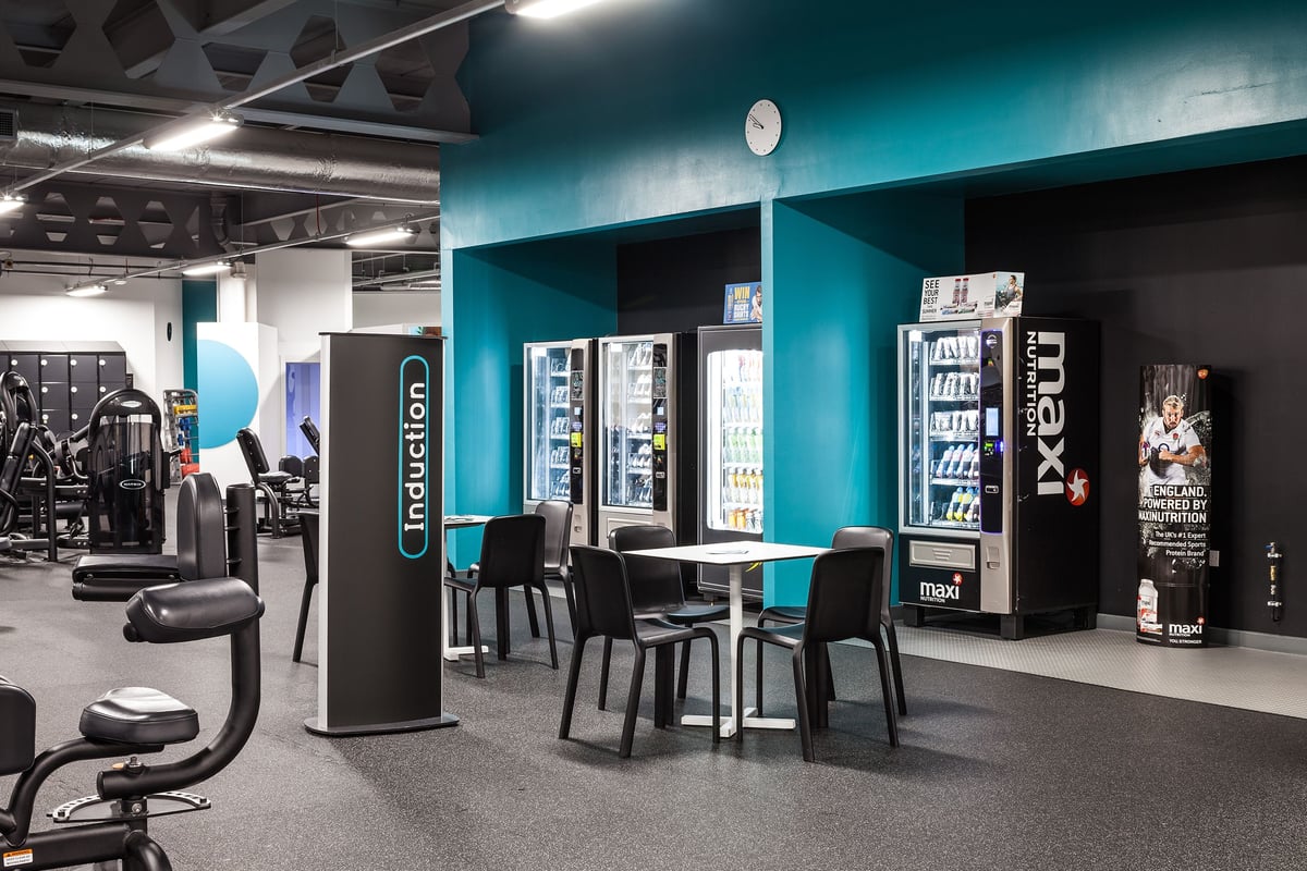PureGym Manchester Stretford: Vending machines, seating area, fitness branding on walls in a gym studio setting.