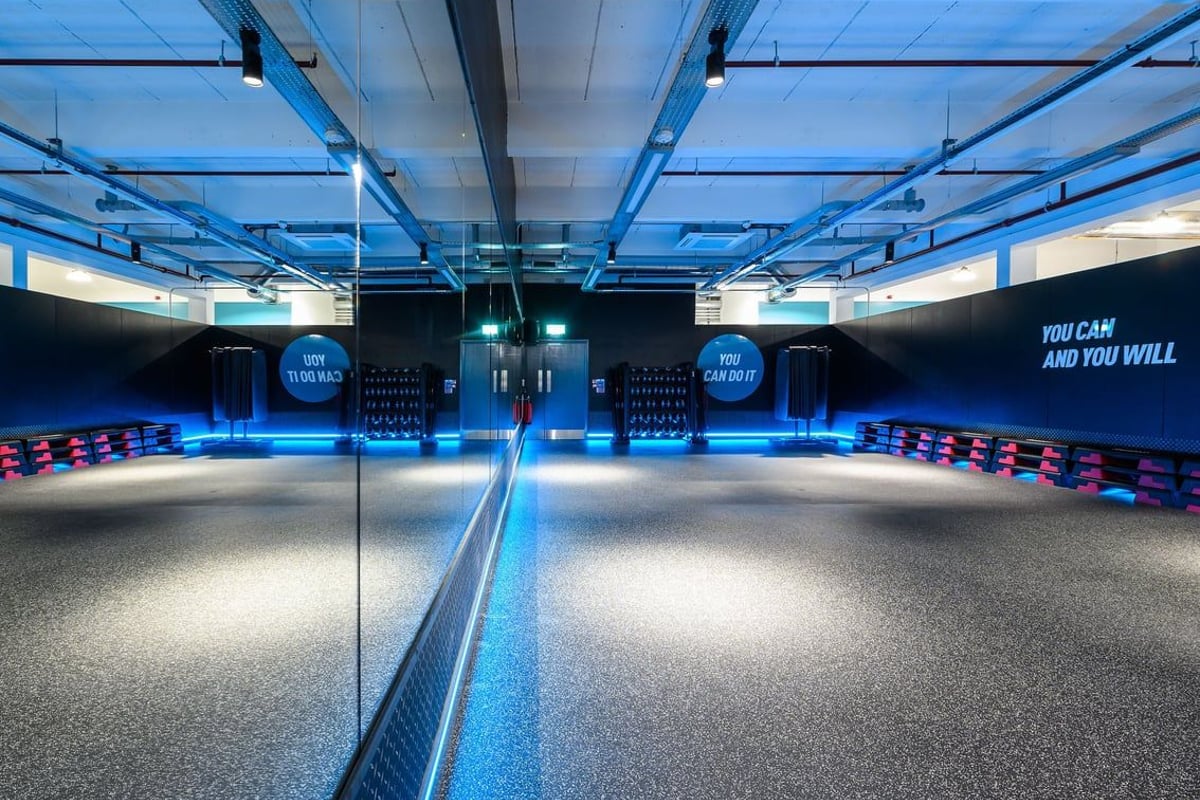 PureGym Northampton Weston Favell: Fitness studio with mirrored wall, free weights rack, and stacks of step platforms.
