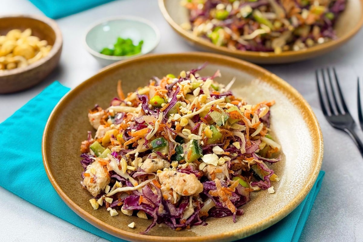 Plates of colourful salad with shredded vegetables, nuts, and pieces of chicken on a blue
