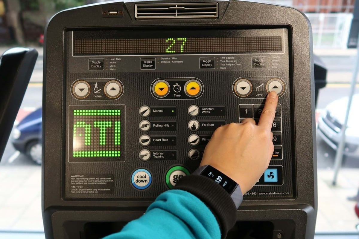 Hand pressing level up button on treadmill control panel with digital display showing 27