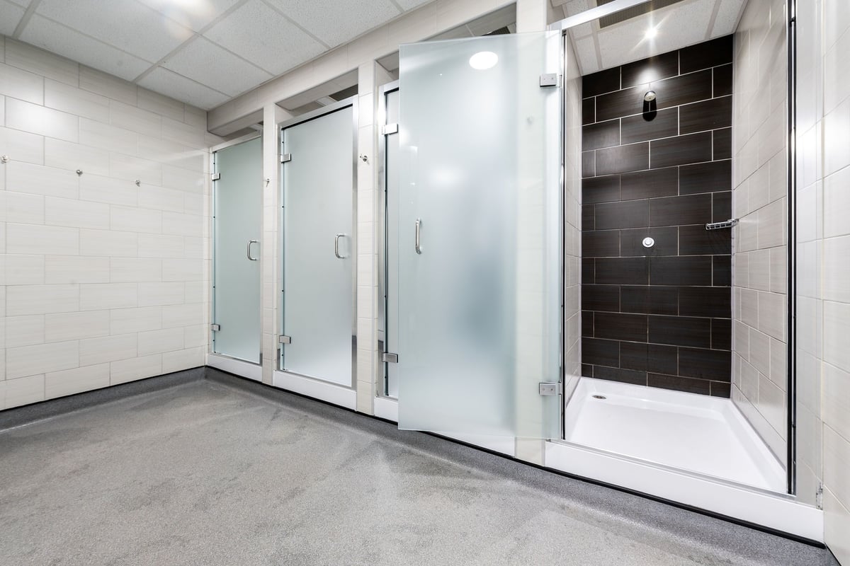 PureGym Warrington Central: Glass shower cubicles, tiled walls, concrete floor - appears to be changing rooms.