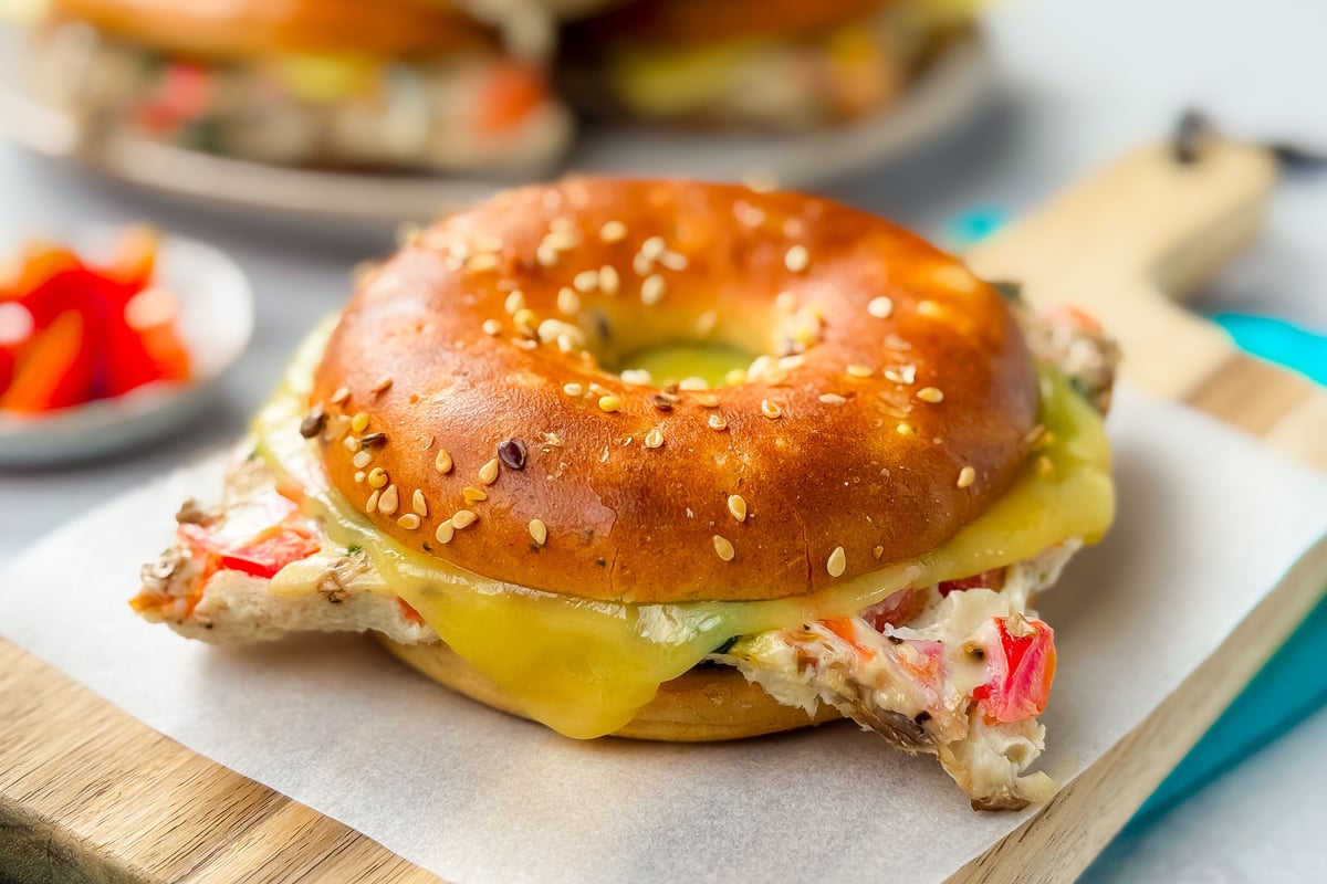Sesame-topped bagel filled with cheese and crab meat on a wooden board