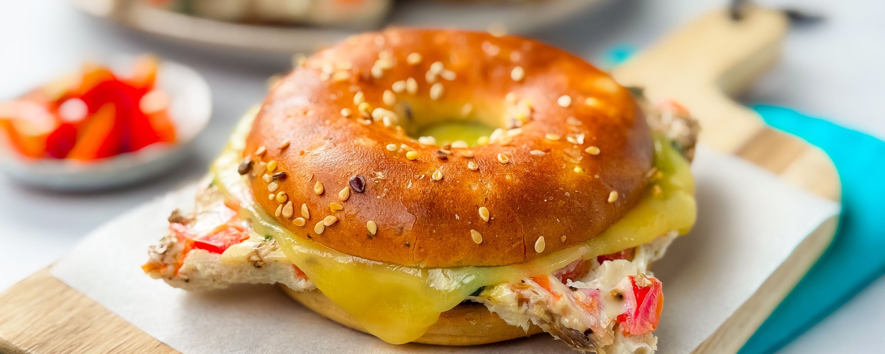 Sesame-topped bagel filled with cheese and crab meat on a wooden board