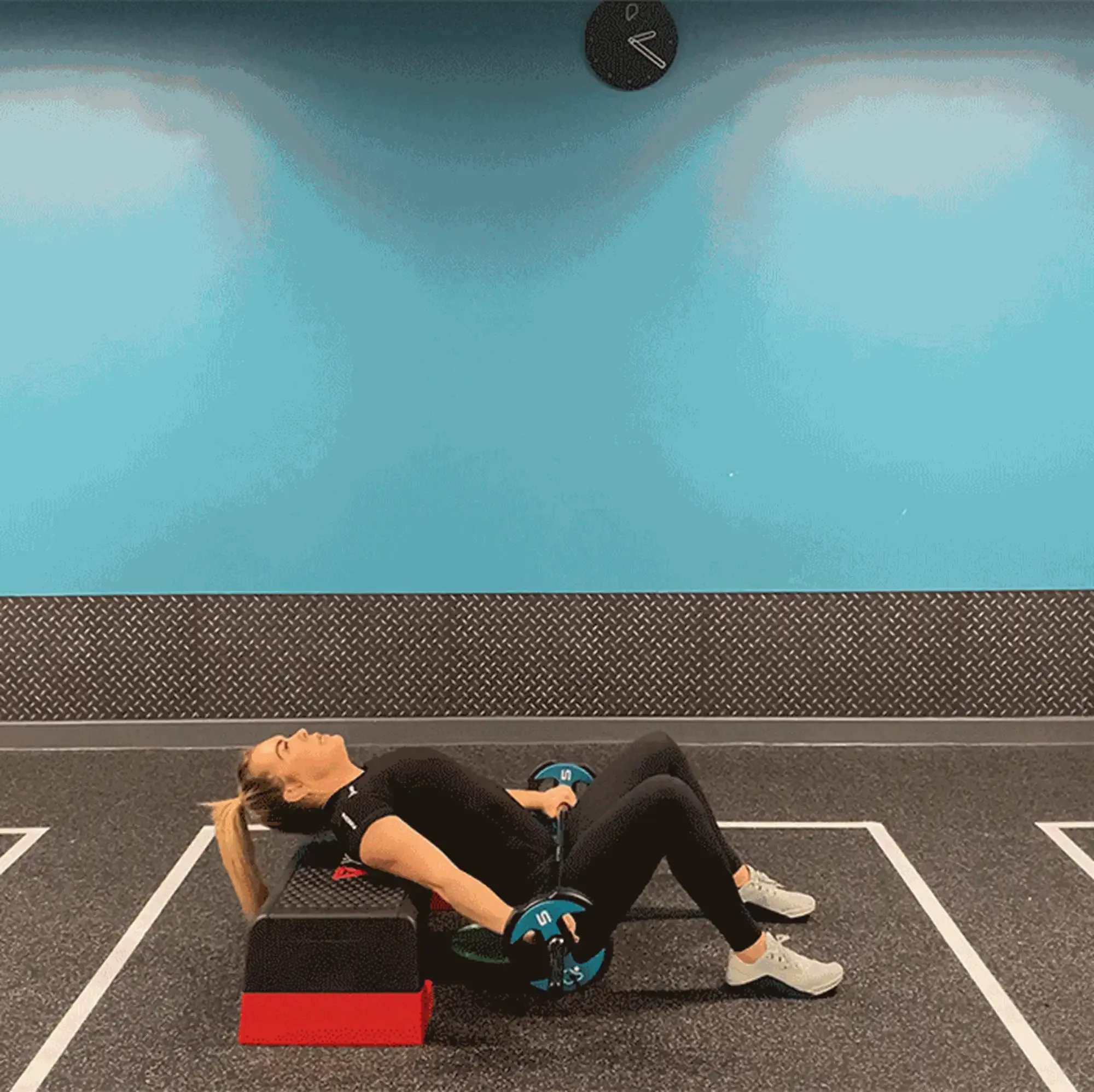 Woman performing hip thrust exercise with barbell on a step platform in gym