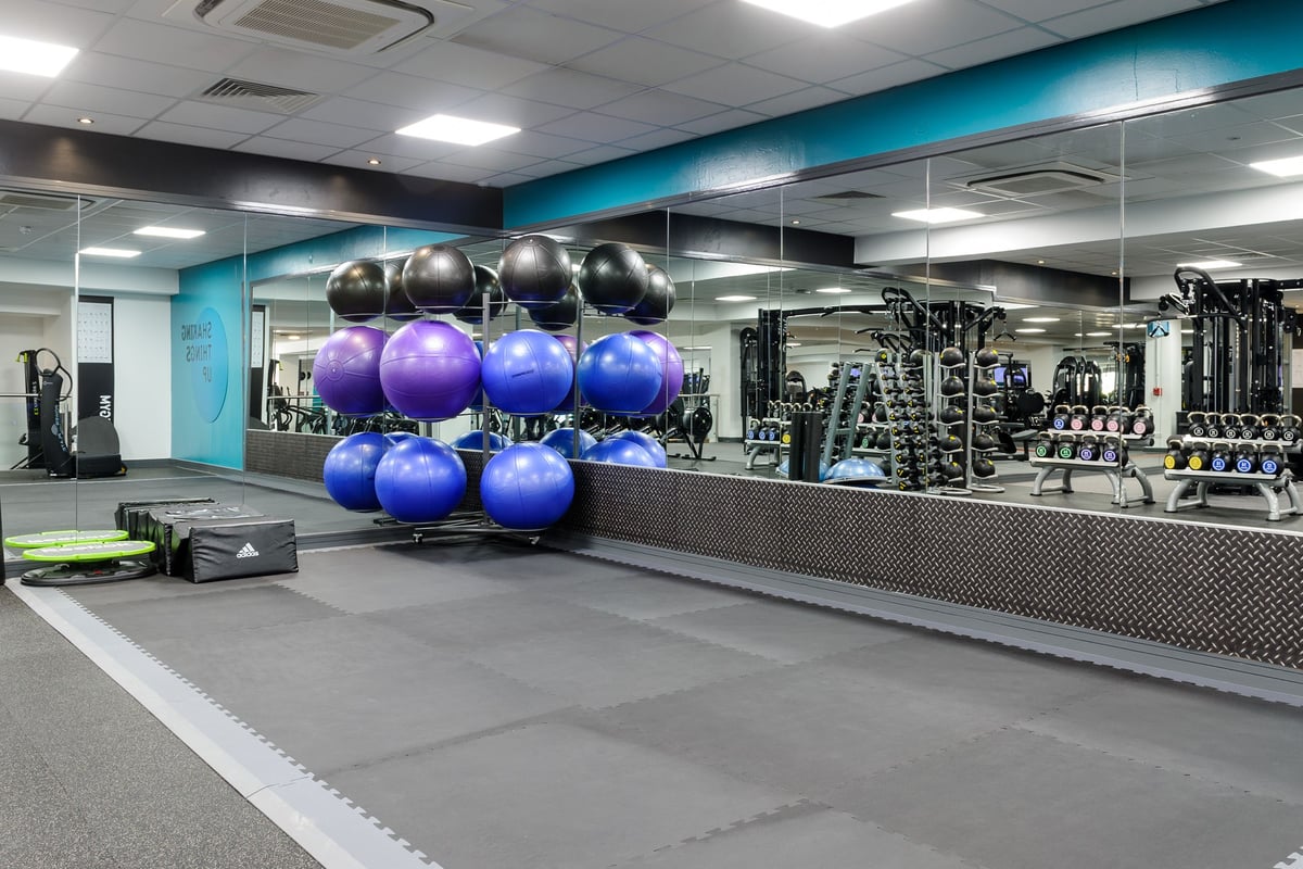 PureGym Billericay: Strength training area with weight balls, dumbbells, cable machines, and rubberized flooring.
