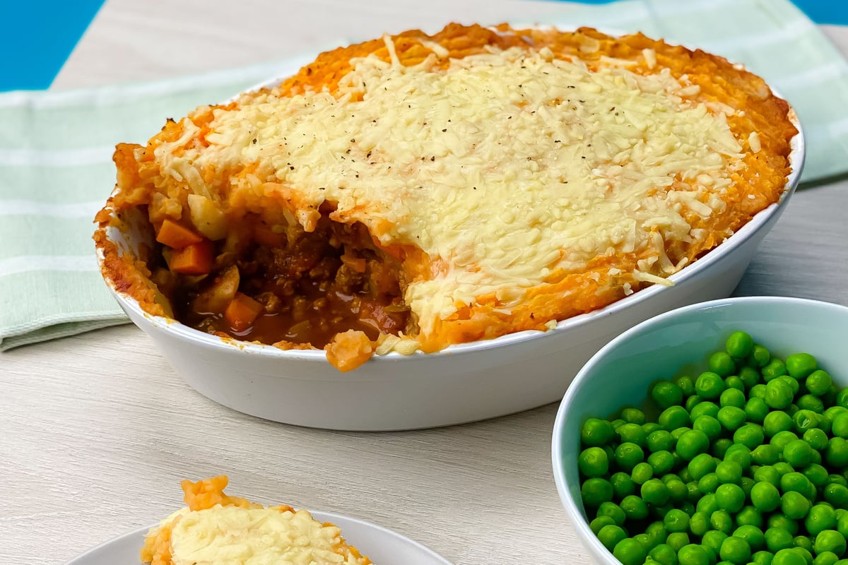 Vegetarian shepherd's pie with sweet potato mash topping in white dish with peas