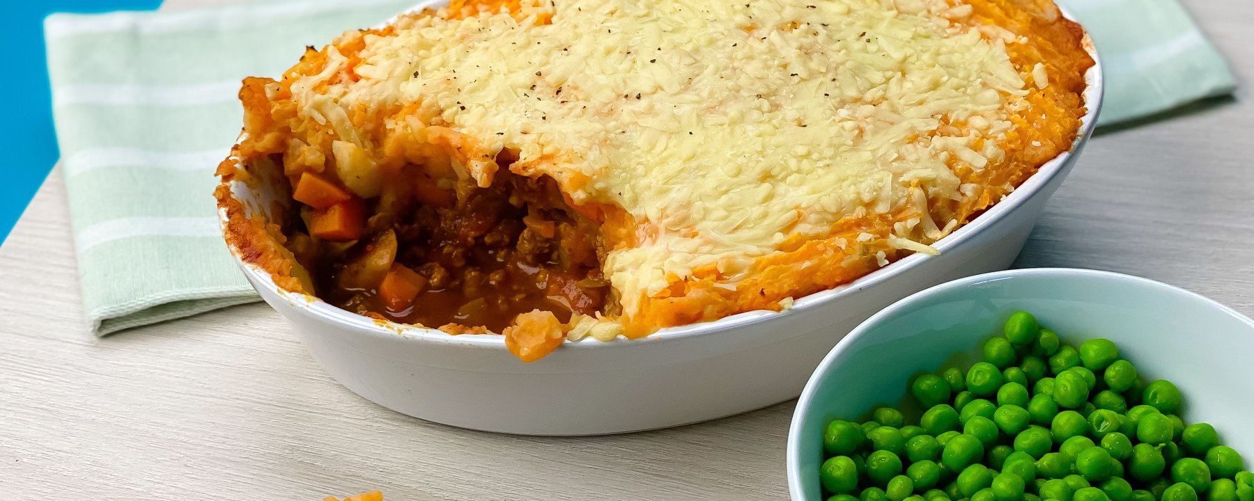 Vegetarian shepherd's pie with sweet potato mash topping in white dish with peas