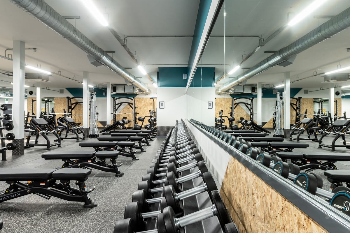 PureGym Macclesfield Silk Road: Rows of benches, weight racks, free weights, and mirrored walls in a modern gym setting.