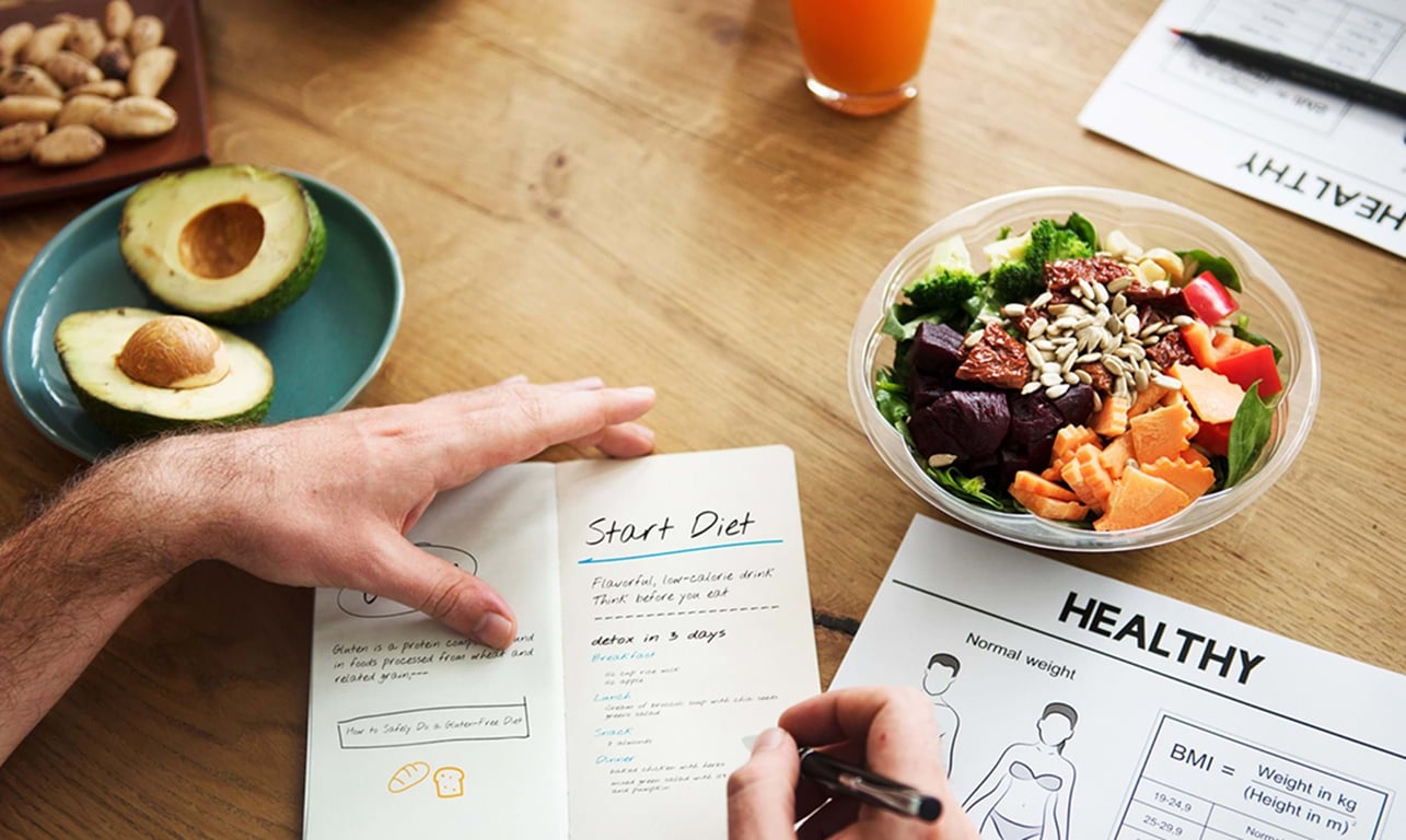 Hand writing diet plan with avocado, nuts, salad bowl, and juice on wooden table