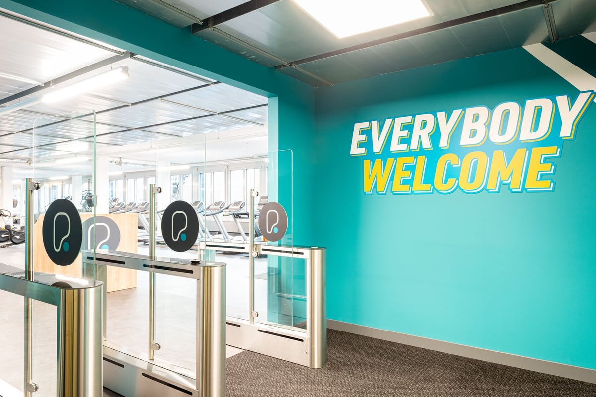PureGym Altstetten: Eingangstore und Wand zum Fitnessstudio mit dem Text „Everybody Welcome“ in Türkis und