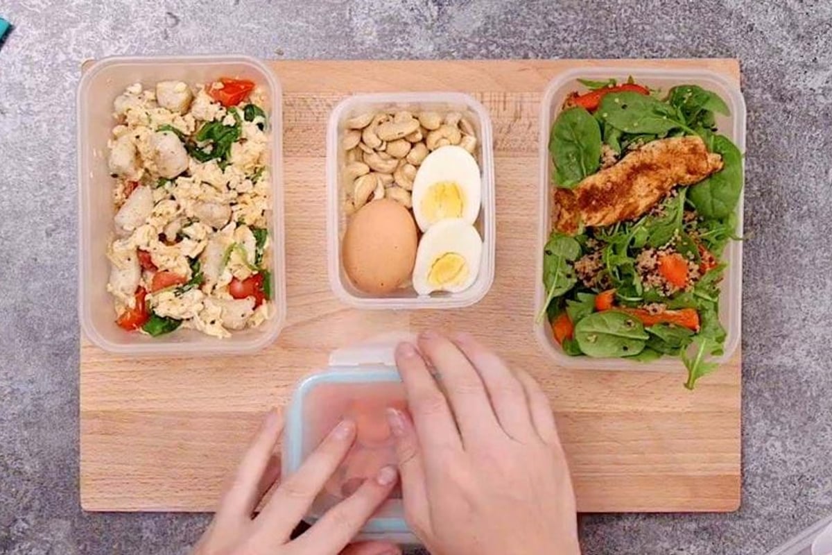Hands arranging meal prep containers with eggs, cauliflower, beans and salad on board