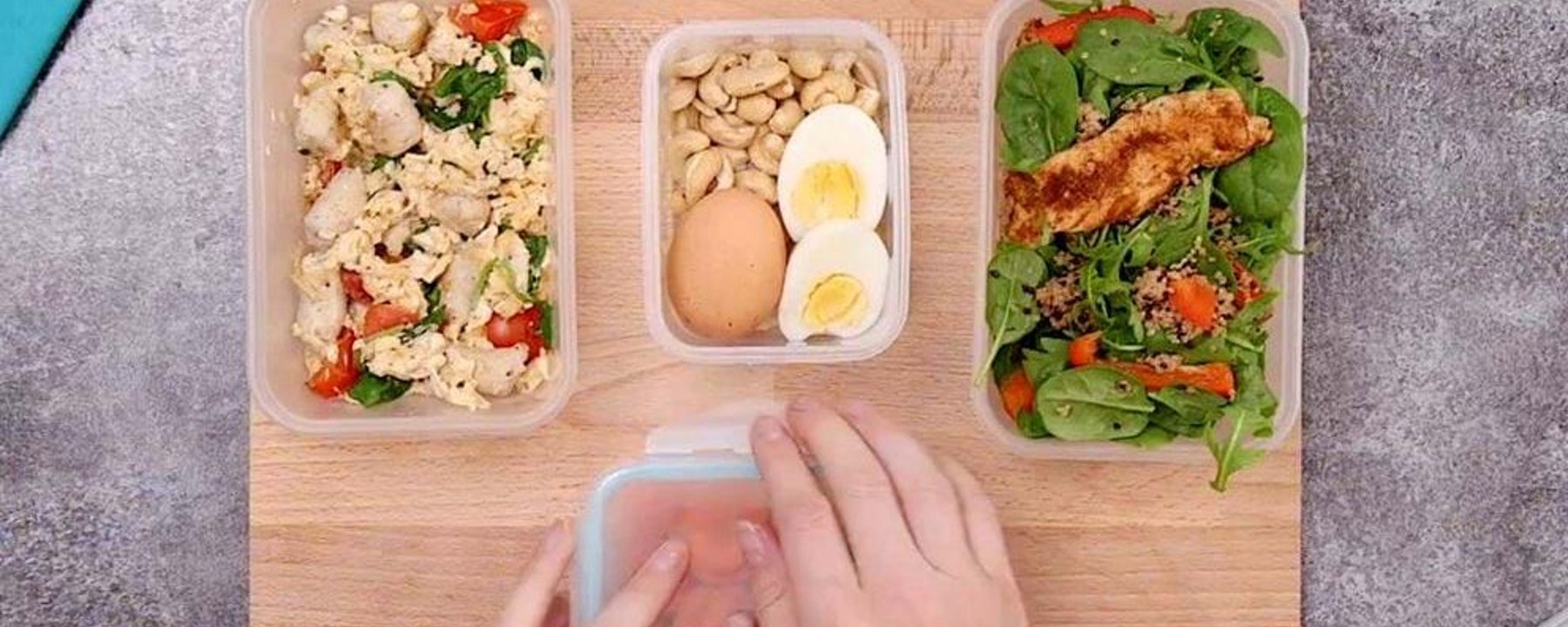 Hands arranging meal prep containers with eggs, cauliflower, beans and salad on board