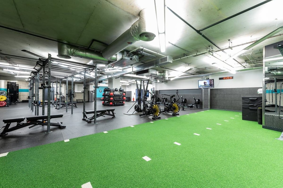PureGym London Aldgate: Weight racks, barbells, free weights, resistance machines, mirrored walls, green turf flooring.
