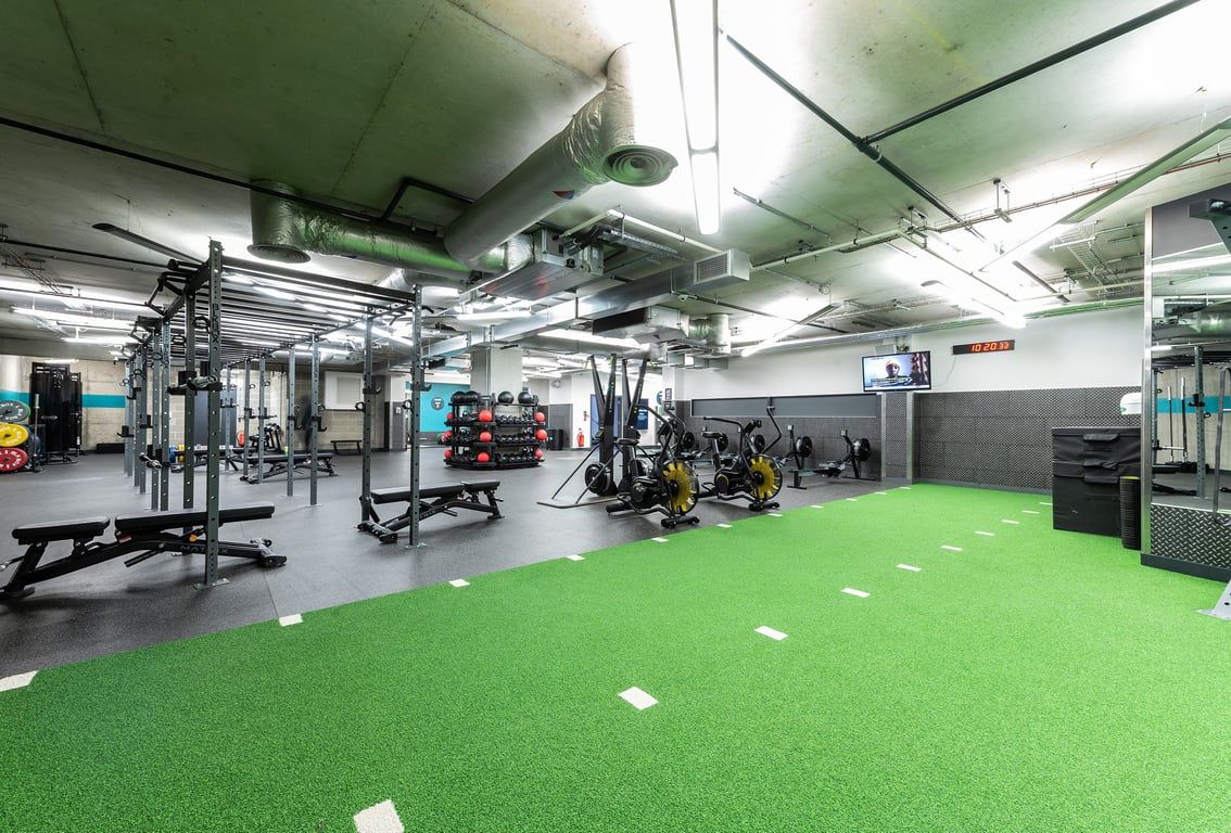 PureGym London Aldgate: Weight racks, barbells, free weights, resistance machines, mirrored walls, green turf flooring.