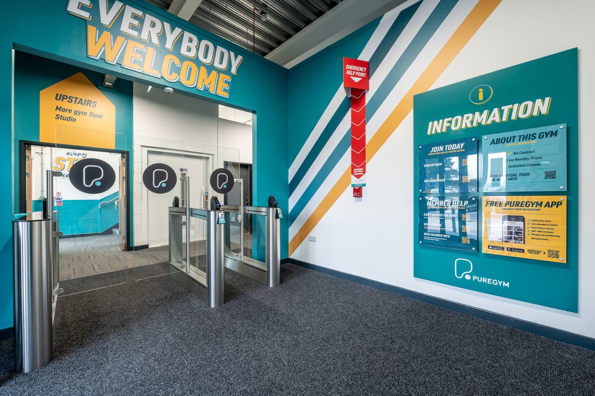 PureGym Plymouth Derriford: Interior space with welcome signage, information board, turnstile entry gates, and flooring.