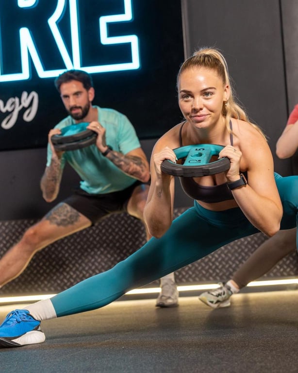 Drei Mitglieder machen seitliche Ausfallschritte mit Gewichten im PureGym-Studio
