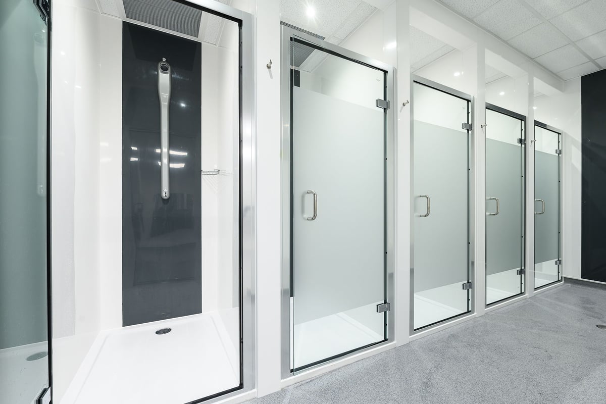 PureGym Romford: Rows of glass shower cubicles in a tiled changing room area.