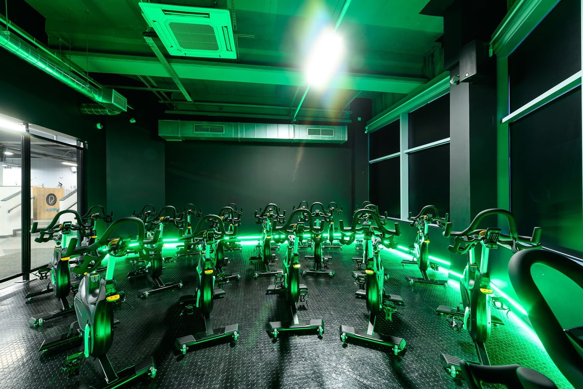 PureGym Leeds City Centre North: Rows of stationary bikes illuminated by neon green lighting inside a fitness studio.