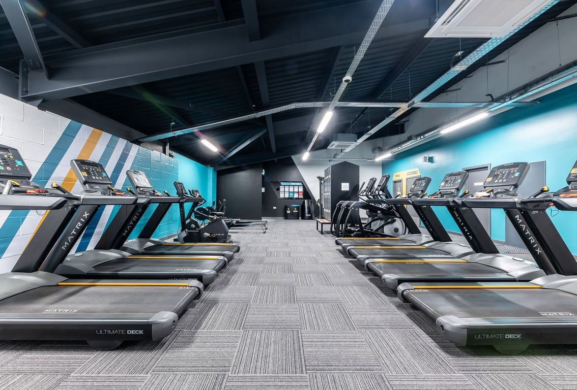 PureGym Redditch Ringway: Rows of modern treadmills amid teal walls, suspended lighting, and geometric wall graphics.