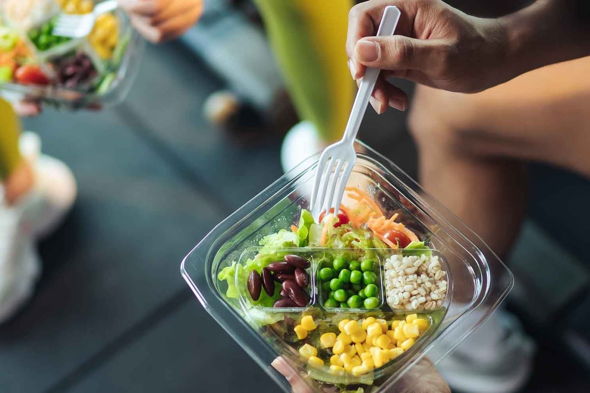 Person hält einen Salatbehälter mit Kopfsalat, Bohnen, Erbsen, Mais und Getreide